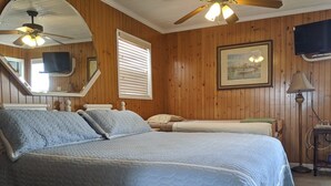 Un dormitorio con una cama grande, un ventilador de techo, un televisor y un cuadro enmarcado en la pared.