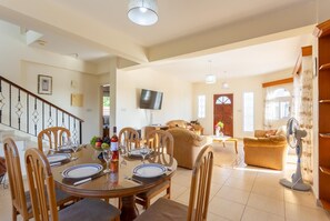 Amplia sala de estar con una mesa de comedor lista para cuatro personas, un sofá y un televisor montado en la pared.