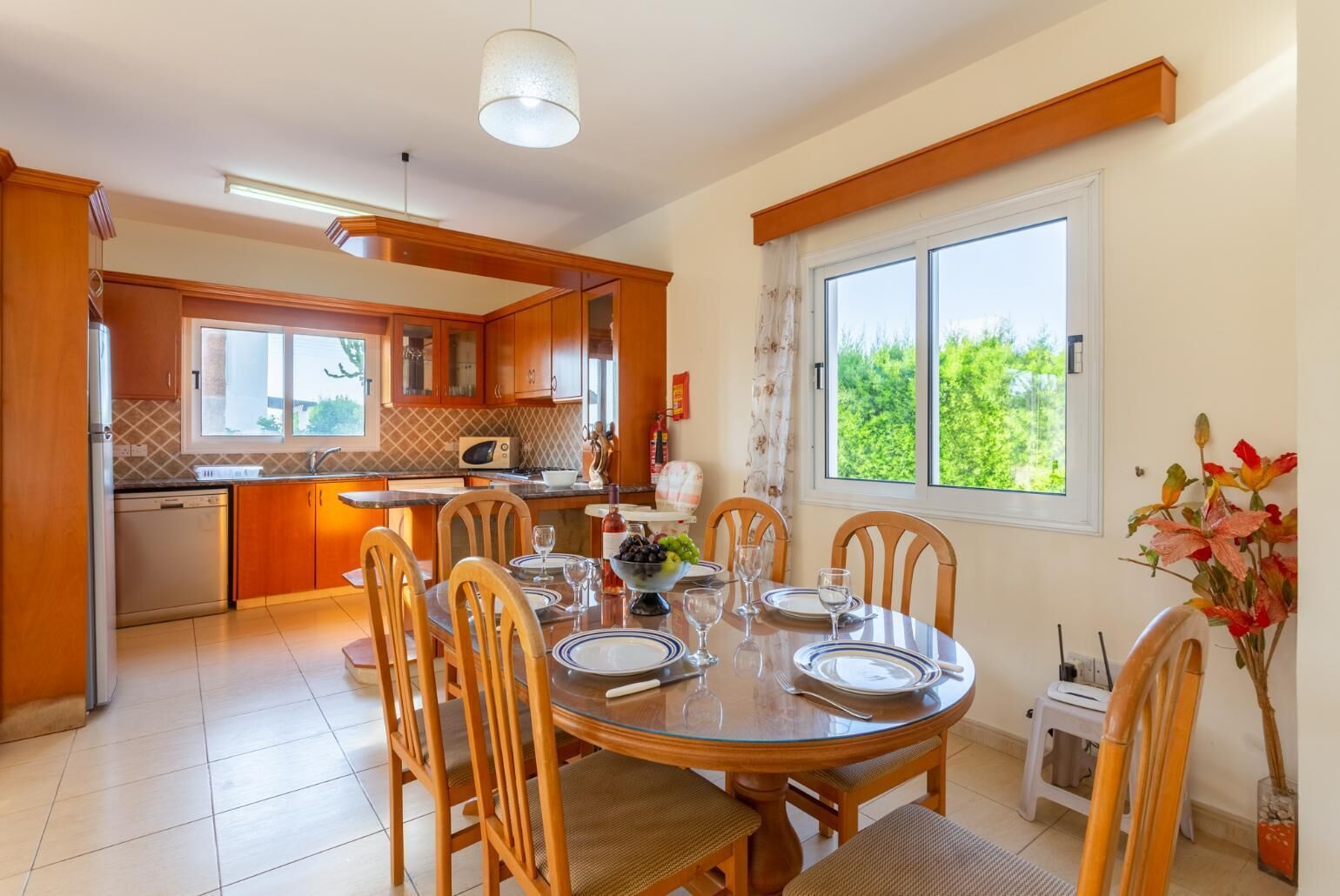 Cozinha moderna com armários de madeira, área de jantar com mesa e cadeiras redondas, e janela com vista para o verde.