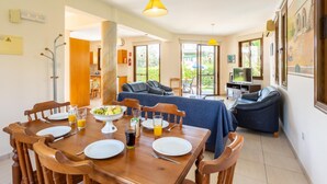 A dining area with a wooden table set for four, a sofa, and a television in the background. - Villa Halima Fostira (Poli Crysochous)