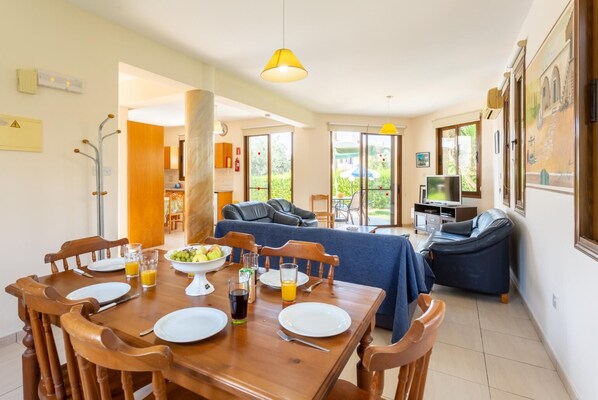A dining area with a wooden table set for four, a sofa, and a television in the background.
