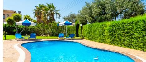 Una piscina de borde curvo, rodeada por un faldón de ladrillo y sillas reclinables azules.