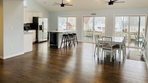 Une cuisine spacieuse équipée d’un réfrigérateur, d’une cuisinière et de tabourets de bar. On y trouve également un coin repas avec une table et des chaises, ainsi qu’un balcon offrant une vue sur le quartier.
