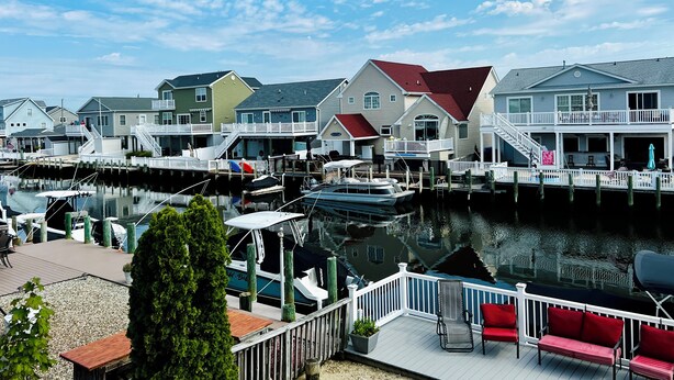 Un port de plaisance avec des bateaux amarrés, des maisons au bord de l’eau et une terrasse en bois avec des sièges d’extérieur.