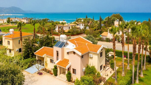 Zona residencial costera con casas de techos anaranjados, rodeada de palmeras y vegetación, con vistas al mar.