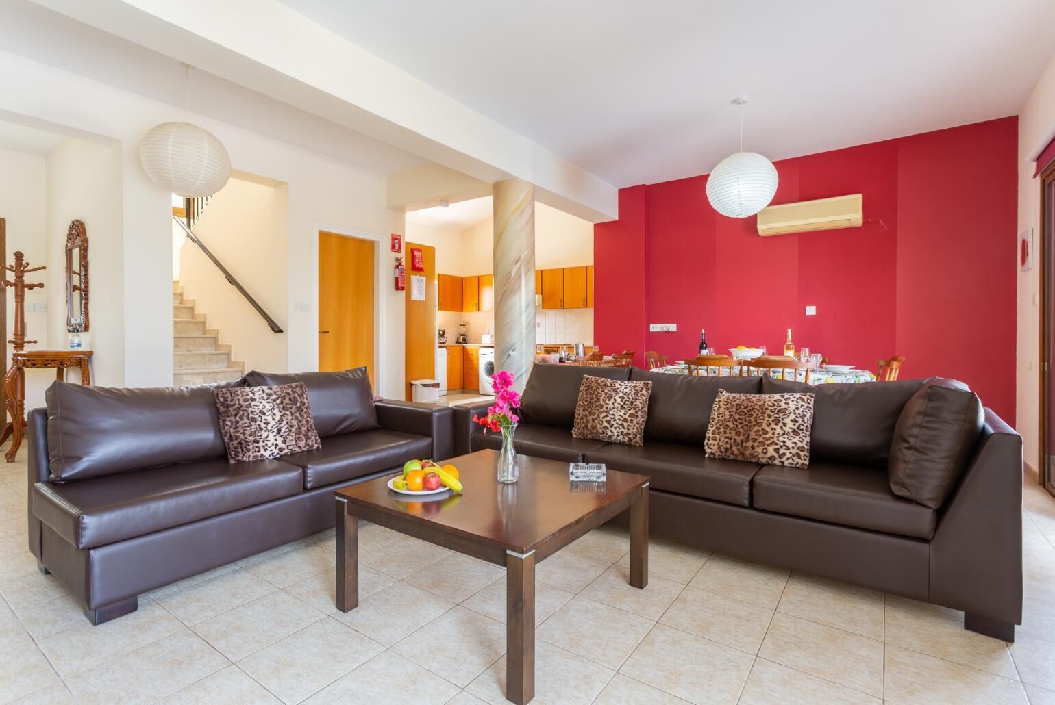 Un salon moderne avec deux canapés en cuir foncé, une table basse sur laquelle sont disposés des fruits et un mur d’accent de couleur rouge.