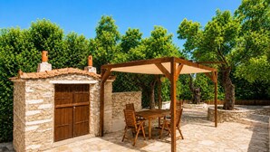 Un edificio de piedra con una puerta de madera, una pérgola con mesa y sillas, y un patio de piedra.
