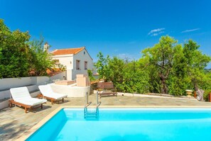 A swimming pool with lounge chairs, a wooden deck, and a white building with a red-tiled roof.