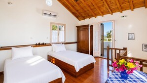 Un dormitorio con dos camas, techo de madera, aire acondicionado, armario y balcón con flores.