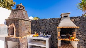 A stone oven and a brick oven with a table and fruit in front, set against a stone wall.
