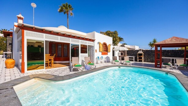 A modern villa with a swimming pool, outdoor seating, and a stone wall.