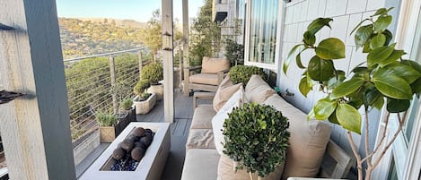 A covered outdoor seating area with a view of the cityscape, featuring a sofa, chairs, and potted plants.