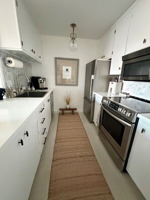 Een moderne keuken met witte kastjes, roestvrijstalen apparatuur, een centraal eiland en een vloerkleed van hout.