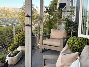 Een balkon met een houten stoel en een kleintje tafeltje, omringd door potplanten en een leuning.