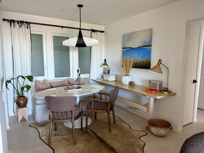 A dining area with a round table, chairs, a hanging light fixture, a painting, and a wooden shelf with decorative items. - Beautiful Tiburon Apt WIth Breathtaking Views Of The Bay (Tiburon)