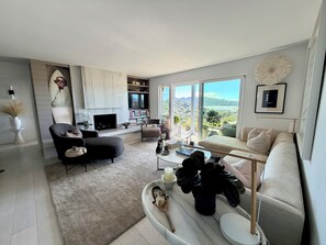 A modern living room with a fireplace, a sofa, a coffee table, and a view of the outdoors. - Beautiful Tiburon Apt WIth Breathtaking Views Of The Bay (Tiburon)