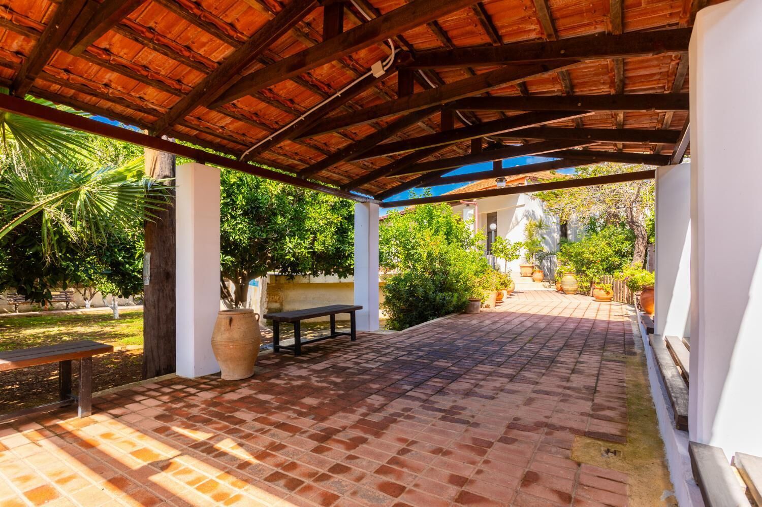 A covered outdoor area with a brick floor, a wooden bench, and a large pot.