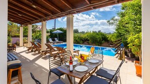 An outdoor pool area with lounge chairs, a dining table set for two, and a view of the pool and surrounding greenery. - Villa Maro Large Private Pool, A/C, WiFi (Kefalas)