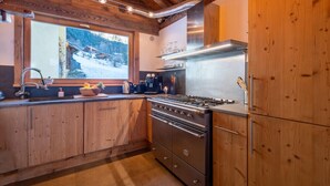 Una cocina con armarios de madera, una estufa de acero inoxidable y un ventanal con vistas a una montaña nevada.