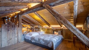 Un dormitorio acogedor en el ático, con vigas de madera a la vista, una cama con manta estampada y una pequeña silla de madera.