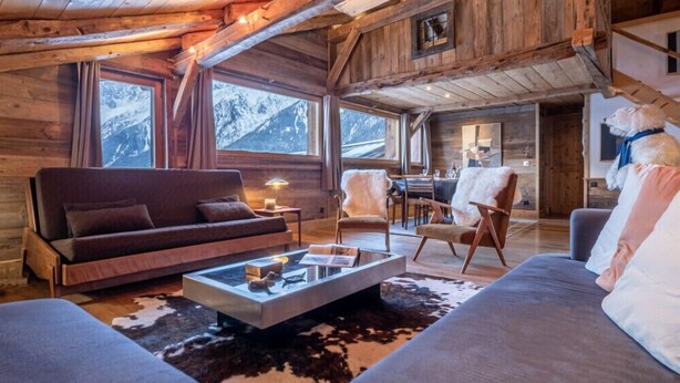 Interior acogedor de una cabaña de troncos con sofá, sillones y zona de comedor.