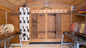 Interior de una cabaña de madera con techo de madera, un soporte para esquíes en la pared y dos bancos.