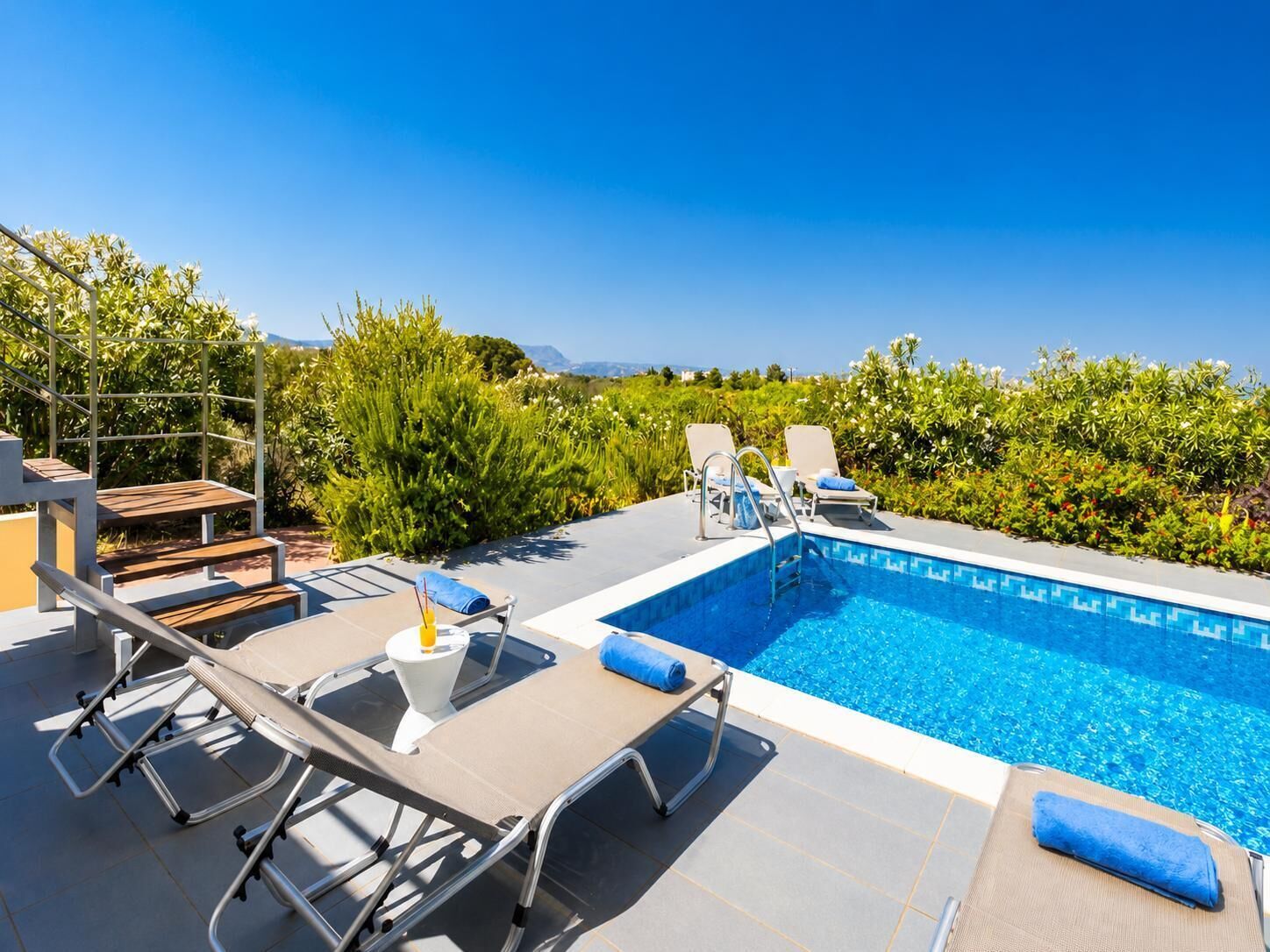 Une piscine sur le toit, avec des chaises longues, une petite table et un escalier.