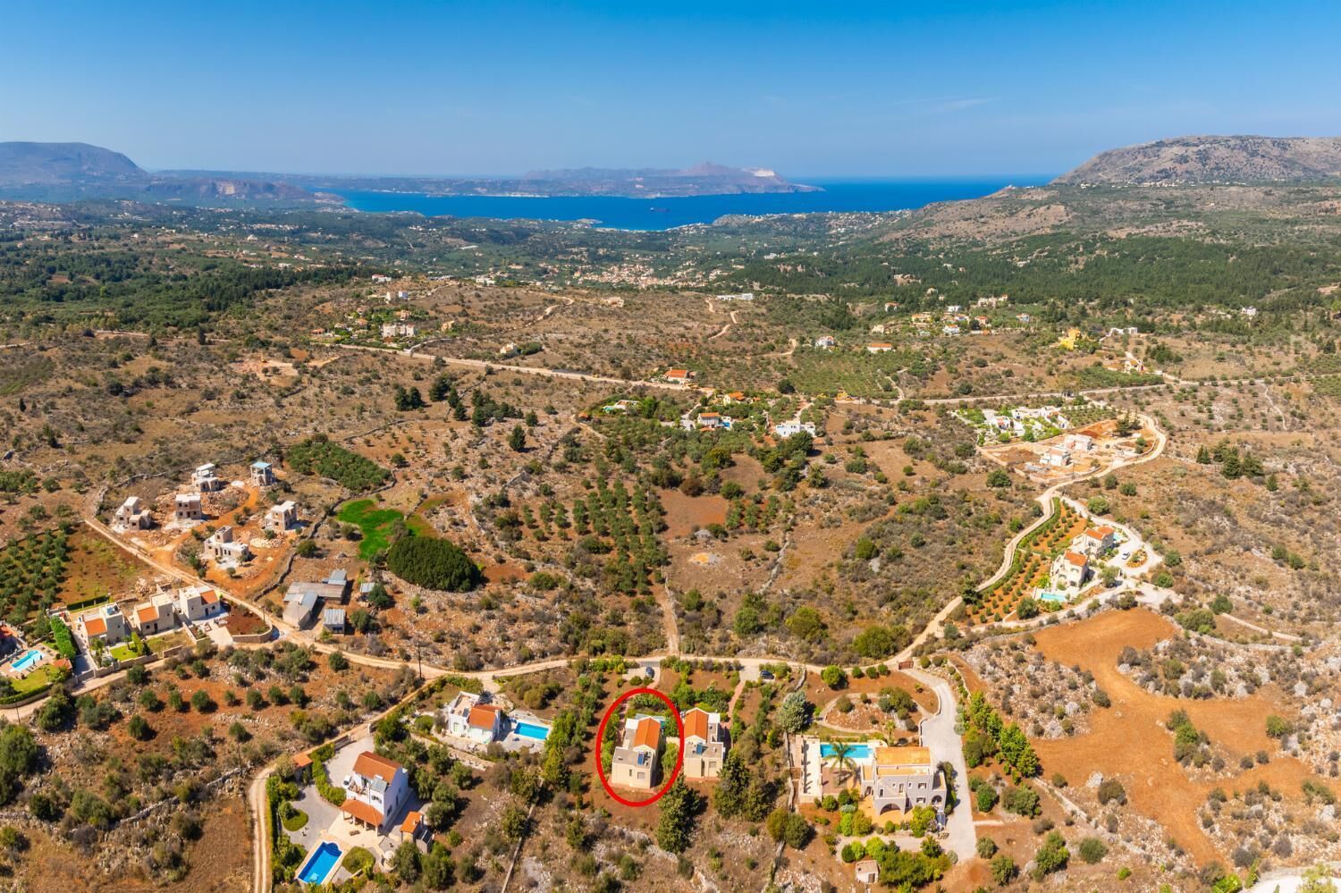 Vista aérea de una zona residencial costera con casas, una piscina y una vista despejada del mar.
