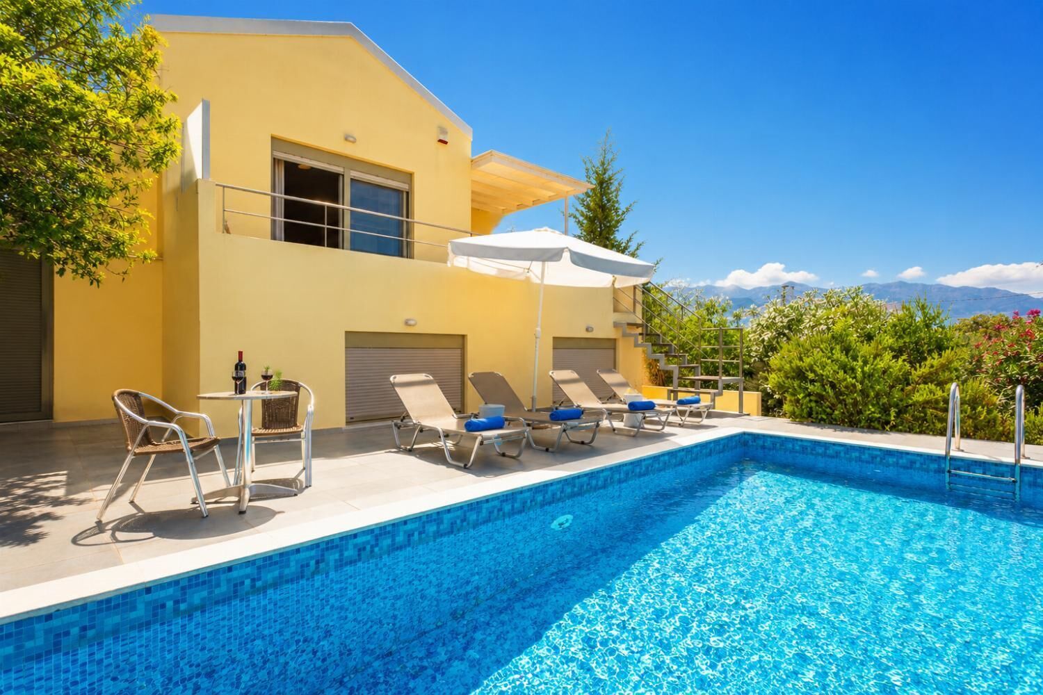 A modern poolside area with a clear blue pool, sun loungers, and a yellow building.