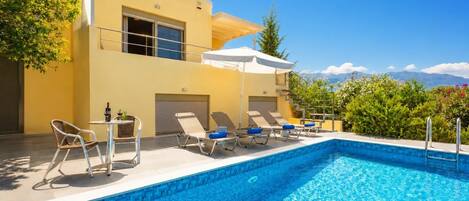 A modern poolside area with a clear blue pool, sun loungers, and a yellow building.