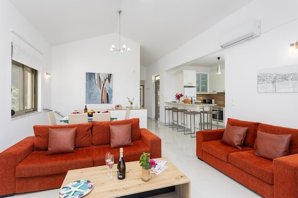 A modern living room with two red sofas, a wooden coffee table, and a dining area with a white table and chairs.