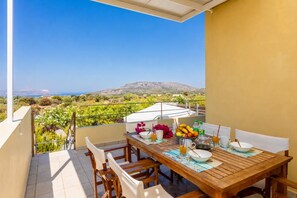 A balcony with a table set for dining, a view of the countryside, and a mountain in the distance.