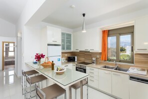 Une cuisine moderne avec des meubles blancs, un îlot central en verre et une fenêtre agrémentée de rideaux orange.