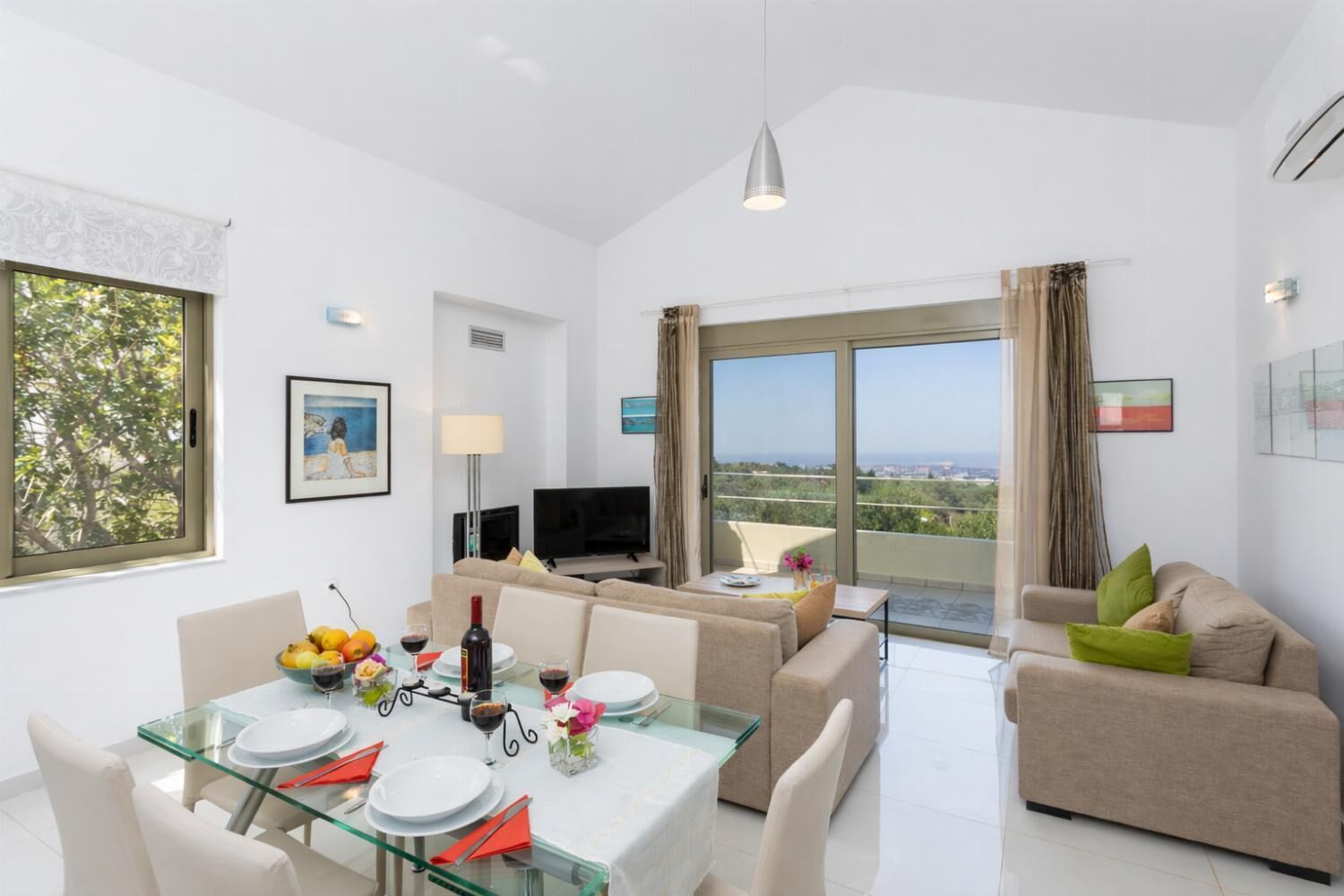 A modern living room with a dining area, a TV, and a balcony with a view.