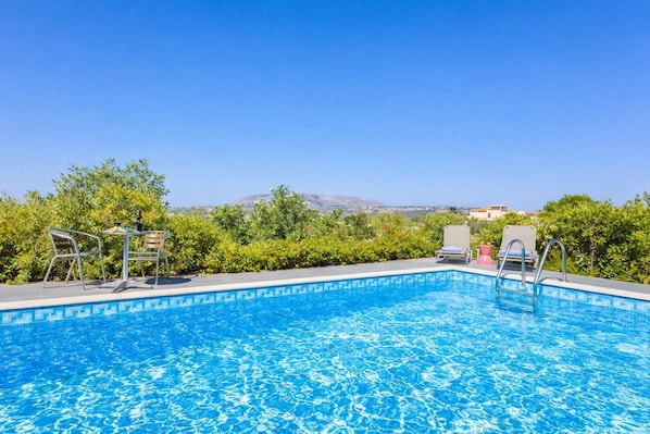 Une piscine à l’eau d’un bleu cristallin, entourée de verdure et offrant une vue sur des collines lointaines.