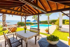 A covered outdoor area with a pool, lounge chairs, and a table with a vase of flowers.