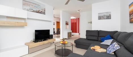 A modern living room with a flat-screen TV, grey sofa, and a ceiling fan.