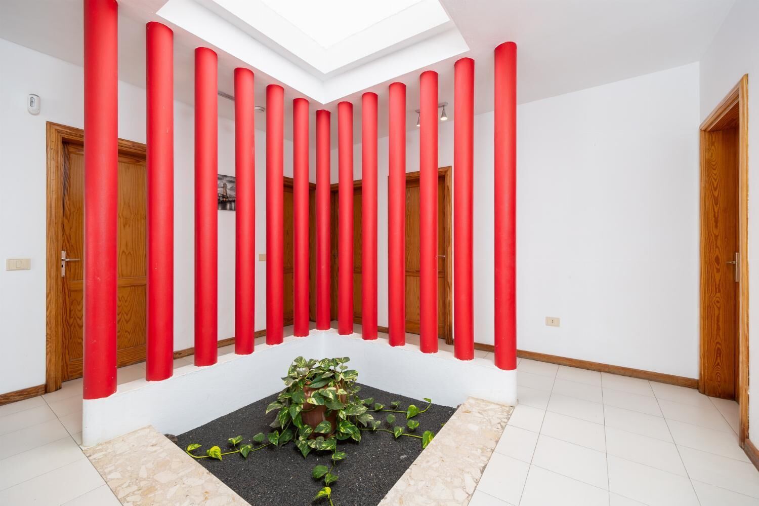 A modern interior with a skylight, red vertical elements, and a potted plant.
