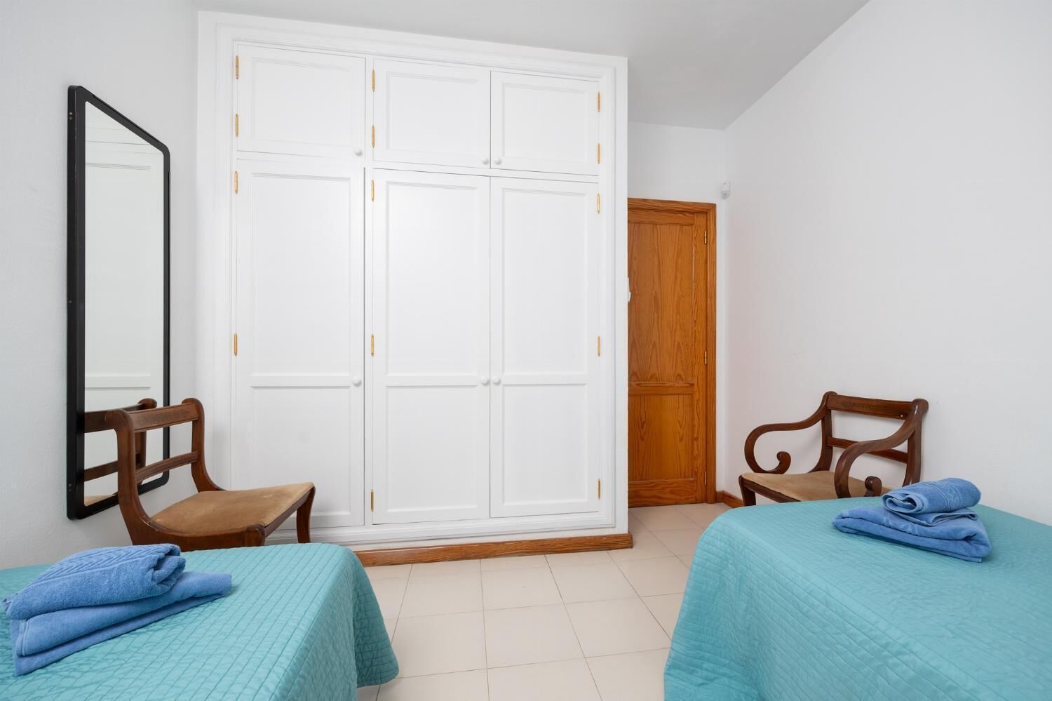 Una habitación con dos camas, un armario de madera, un espejo y una puerta de madera.