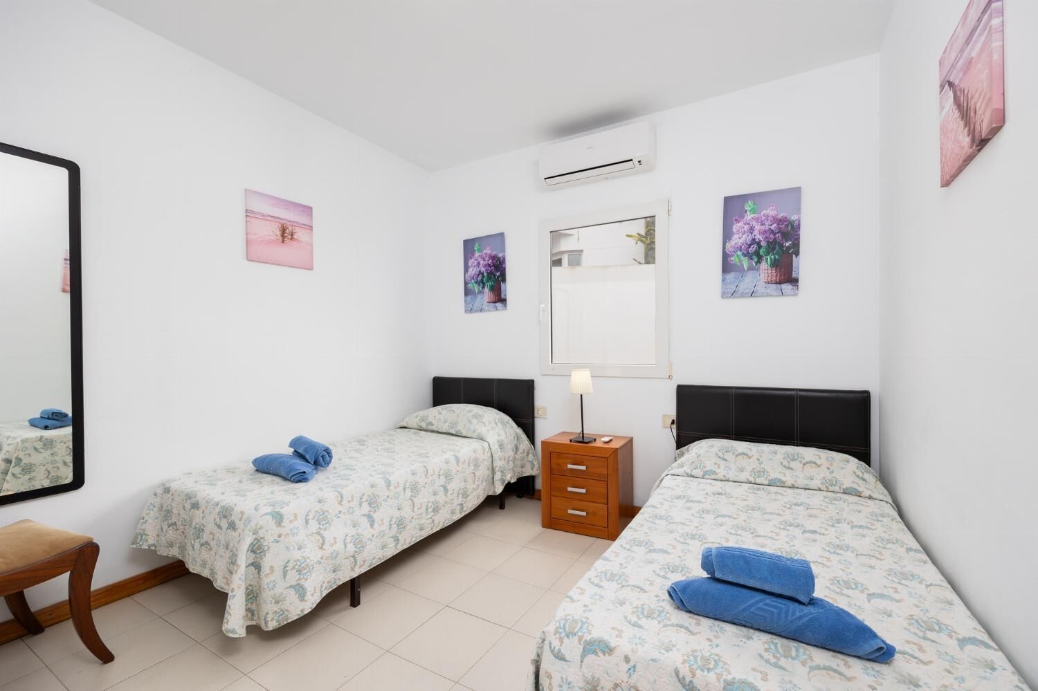 Een slaapkamer met twee eenpersoonsbedden, een houten nachtkastje, een spiegel en wanddecoratie.