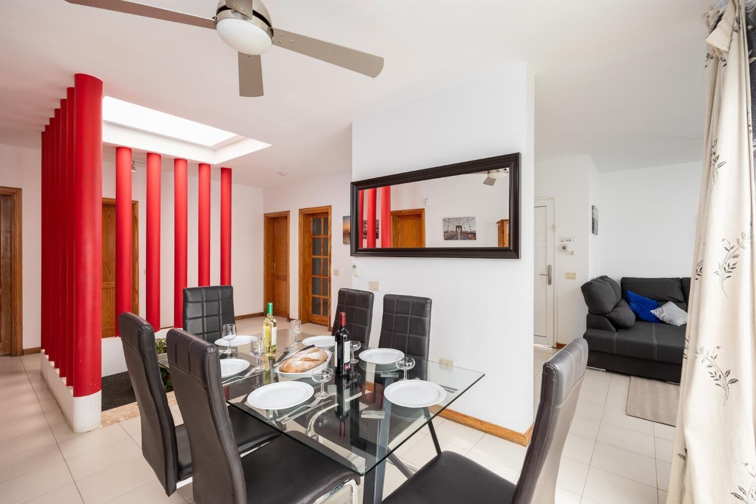A modern dining area with a glass table, black chairs, and red accents on the walls.