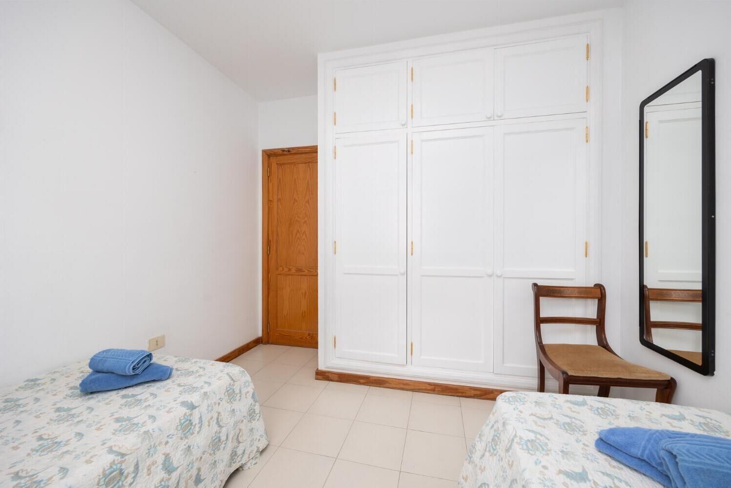 A bedroom with two single beds, a wooden wardrobe, a wooden chair, and a large mirror.