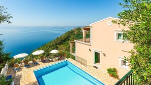 Un edificio de dos pisos con piscina, mobiliario exterior y vista al mar.