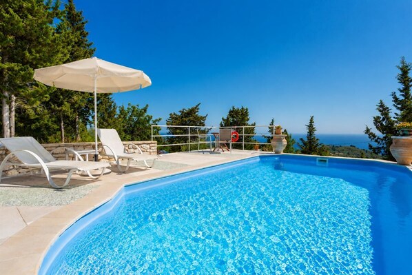 Une piscine dotée de chaises longues et d’un parasol, entourée d’arbres et offrant une vue dégagée sur l’océan.