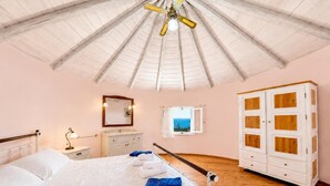 Een slaapkamer met een bed, nachtkastje, dressoir, kledingkast, plafondventilator en een raam met uitzicht.