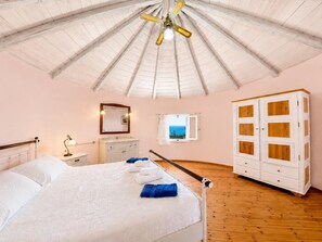Un dormitorio con cama, mesita de noche, cómoda, armario, ventilador de techo y ventana con vistas.
