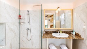 Een badkamer met een douchecabine van glas, een wand betegeld met marmer, een wastafel met een granieten aanrechtblad en een spiegel met verlichting.