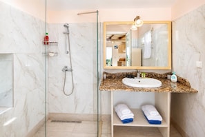 A bathroom with a glass-enclosed shower, a marble-tiled wall, a sink with a granite countertop, and a mirror with a light fixture.