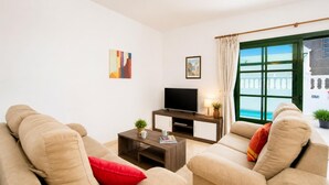 Una sala de estar con dos sofás color beige, una mesa de centro, un televisor de pantalla plana y una ventana con vista a un edificio.