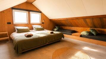 A cozy attic bedroom with a bed, a sofa, and a large woven rug.